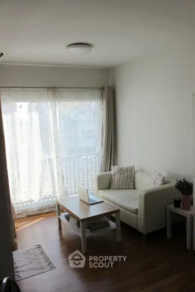 Cozy living room with natural light and balcony access, featuring a white sofa and wooden flooring.