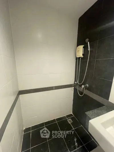 Modern bathroom with sleek black and white tiles and a wall-mounted shower unit.