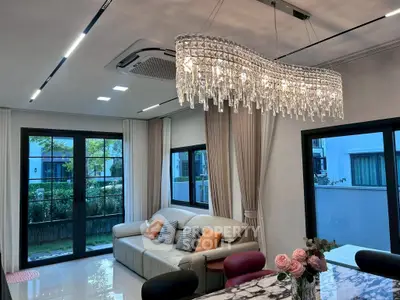 Luxurious living room with elegant chandelier and modern decor, featuring large windows and a cozy sofa.