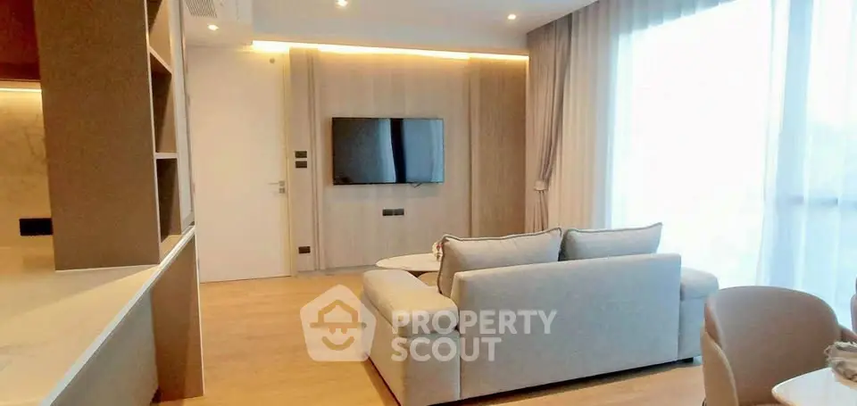 Modern living room with sleek design and natural light, featuring a wall-mounted TV and cozy seating area.