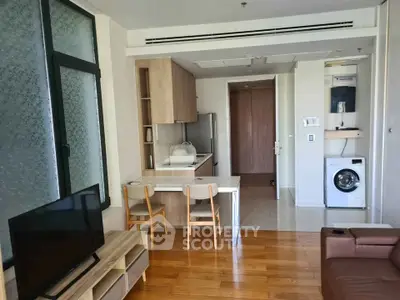 Modern living room with open kitchen and washing machine, featuring wooden flooring and contemporary furniture.