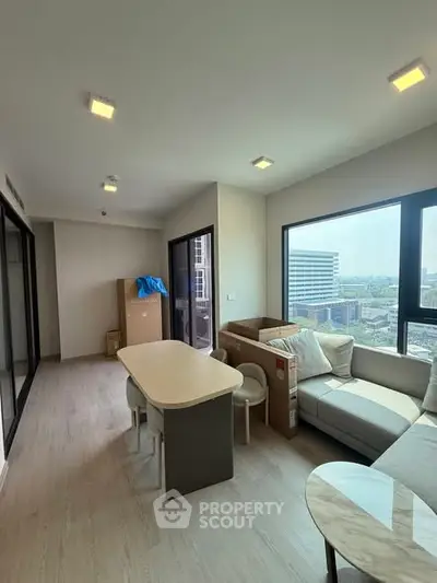 Modern living room with large windows and city view, featuring a cozy sofa and dining area.