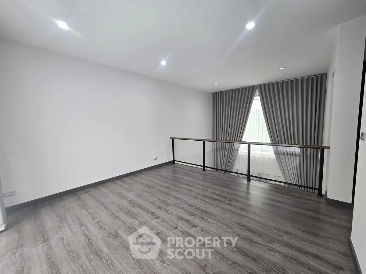 Spacious modern room with wooden flooring and large window with elegant curtains.