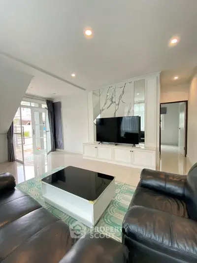 Spacious modern living room with sleek black leather sofas and large TV, perfect for relaxation.