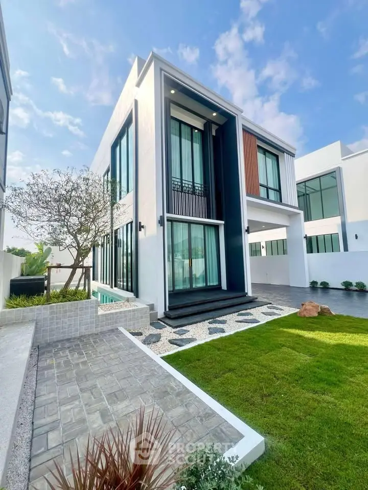 Modern luxury home with sleek design and lush green lawn under a clear blue sky.