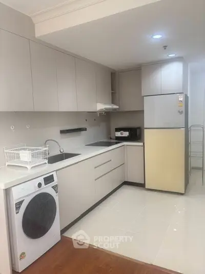 Modern kitchen with sleek cabinetry, washing machine, and fridge in a stylish apartment.