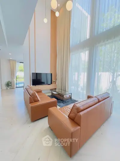 Luxurious high-ceiling living room with leather sofas and large windows offering natural light.
