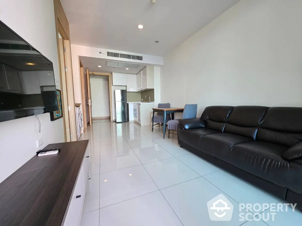 Spacious and modern living room seamlessly connected to an open layout kitchen, featuring sleek white tiles and a plush leather sofa.