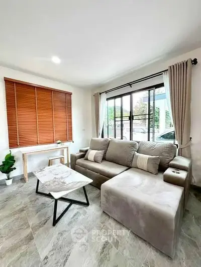Modern living room with stylish gray sofa and marble coffee table, featuring large windows and elegant decor.