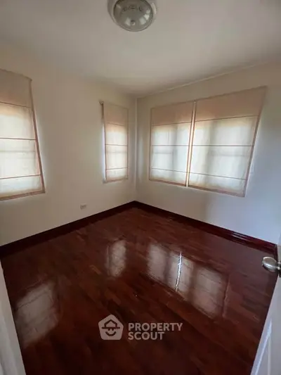 Spacious empty bedroom with polished wooden floors and large windows.