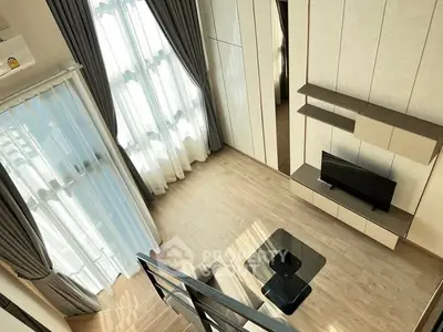 Modern living room with high ceiling and large windows, featuring stylish furniture and elegant decor.