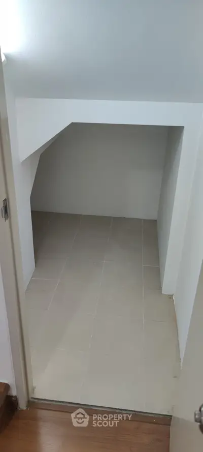 Compact storage space with tiled flooring and sloped ceiling, ideal for extra storage needs.