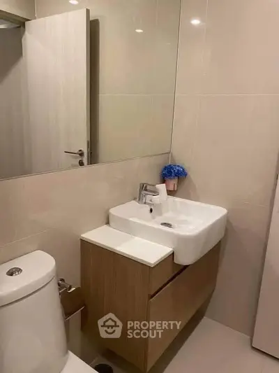 Modern bathroom with sleek sink and toilet, featuring elegant beige tiles and a touch of decor.