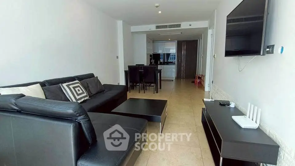 Spacious modern living room with sleek black furniture and open kitchen layout.
