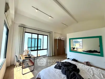Spacious bedroom with large window and modern decor, featuring a cozy bed and stylish workspace.