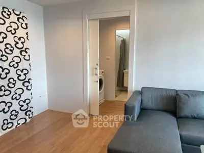 Modern living room with wooden flooring and stylish gray sofa, featuring a washing machine in the background.