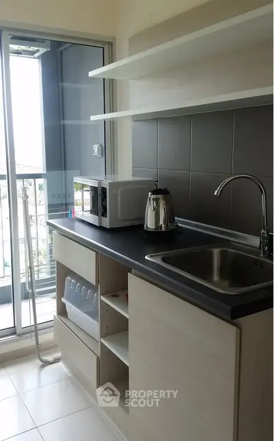 Modern kitchen with sleek countertops, stainless steel sink, and balcony view, perfect for urban living.