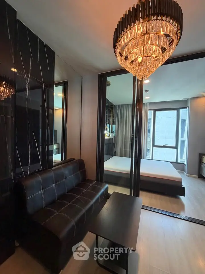 Luxurious modern living room with elegant chandelier and sleek black sofa, adjacent to a stylish bedroom.