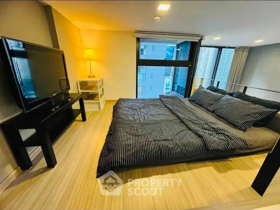Modern bedroom with large windows and city view, featuring a sleek TV setup and stylish decor.