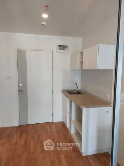 Modern compact kitchen with wooden flooring and white cabinetry in a cozy apartment.