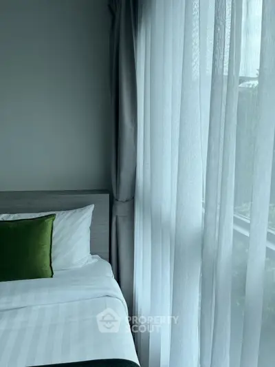 Cozy bedroom with elegant curtains and green accent pillow, perfect for relaxation.