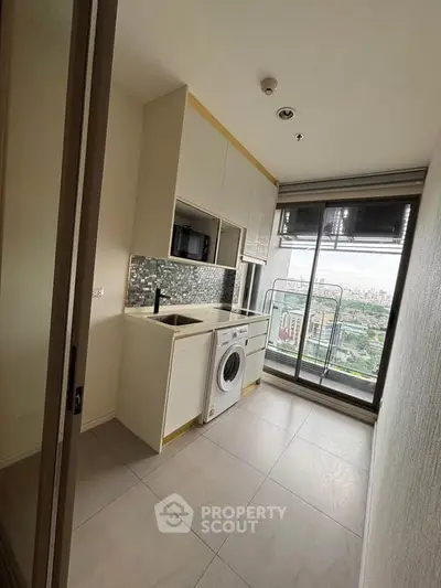 Modern compact kitchen with washing machine and city view from balcony.