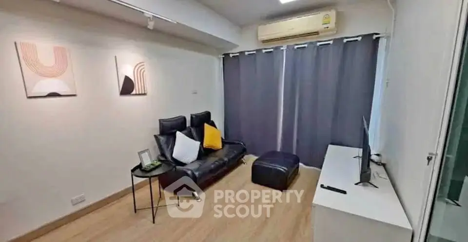 Modern living room with sleek black sofa, wall art, and air conditioning, perfect for cozy relaxation.