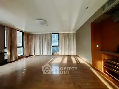 Spacious sunlit living room with large windows and wooden flooring