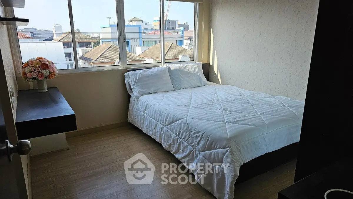Cozy bedroom with large window offering city views and natural light, featuring a comfortable bed and elegant decor.