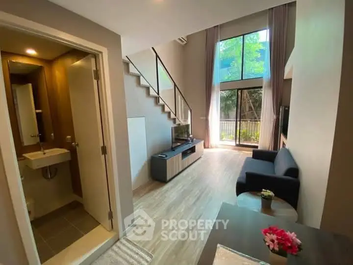 Modern duplex living room with high ceilings and large windows overlooking greenery.