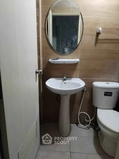 Compact bathroom with pedestal sink and round mirror, ideal for small spaces.
