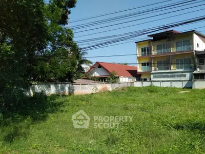 Spacious green plot with potential for development, surrounded by residential buildings and lush trees.
