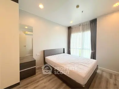 Modern bedroom with large window and wooden flooring in a bright apartment.