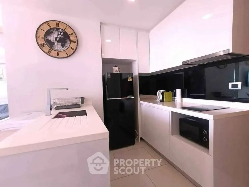 Modern kitchen with sleek white cabinets and black appliances, featuring a stylish wall clock.
