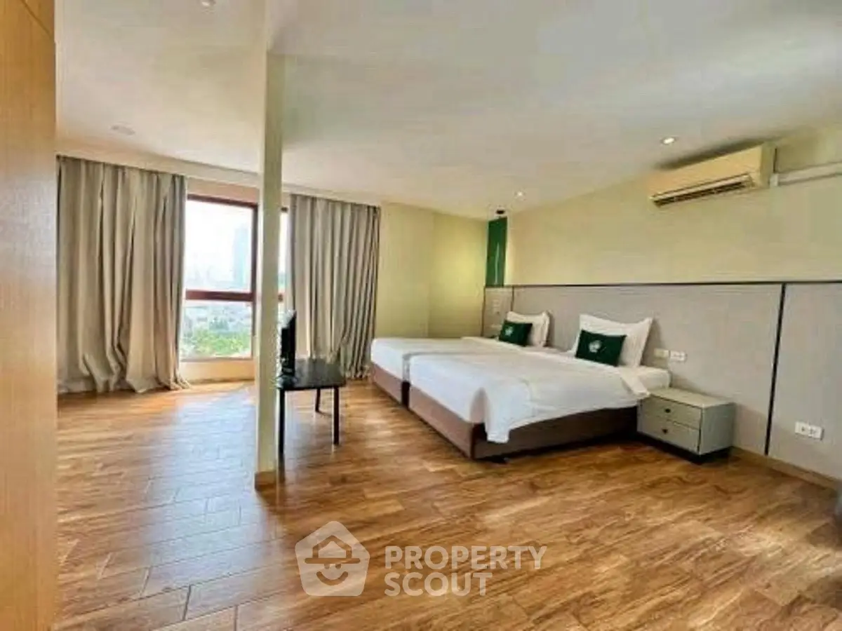 Spacious bedroom with twin beds and city view, featuring modern wooden flooring.