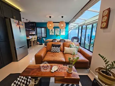 Stylish modern living room with leather sofa and open kitchen layout, featuring natural light and chic decor.