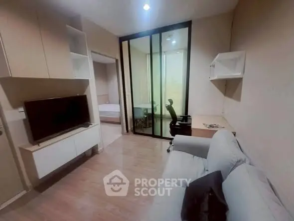 Modern living room with sliding glass doors leading to a cozy bedroom, featuring sleek furniture and a work desk.