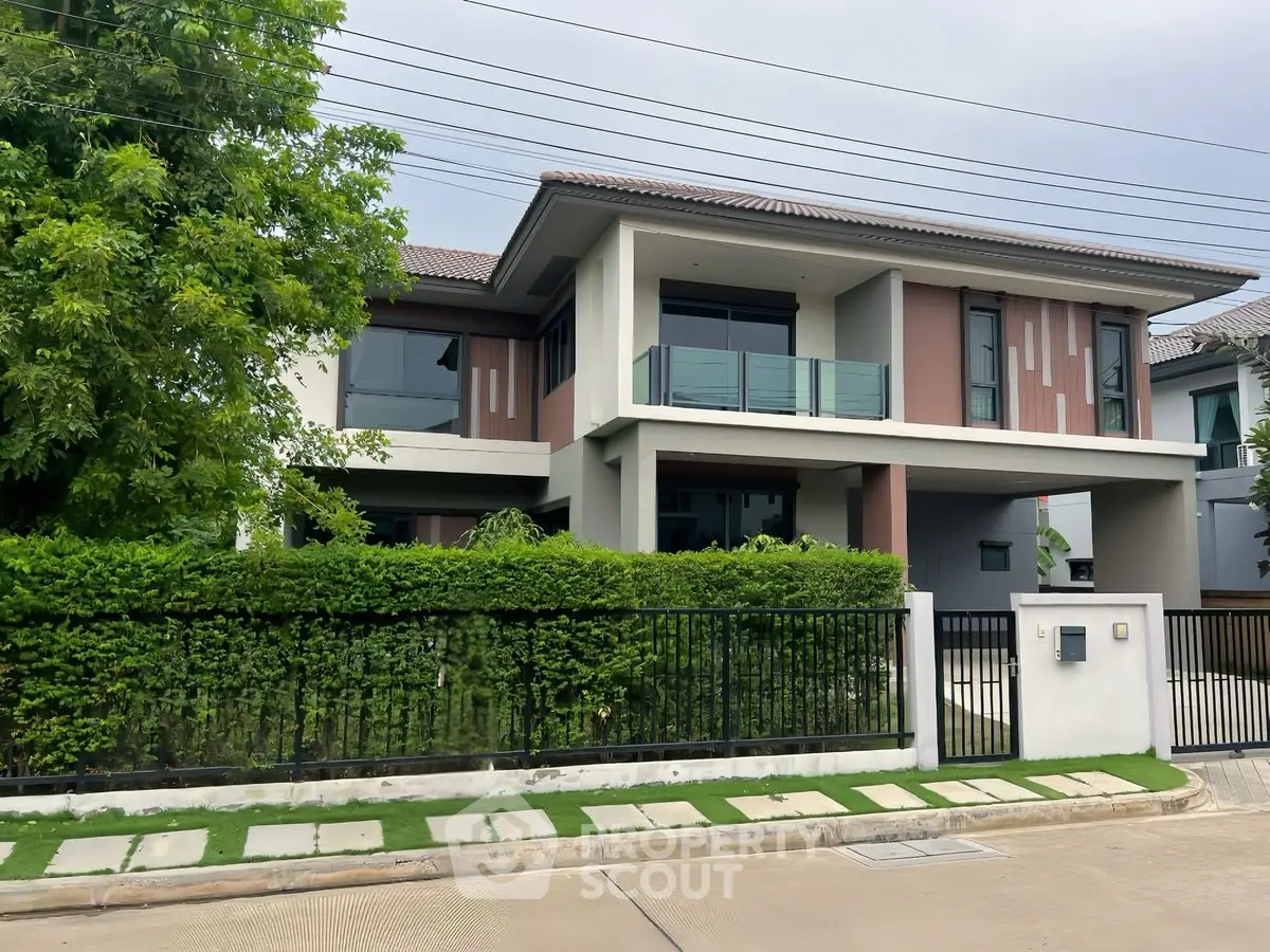 Modern two-story house with lush greenery and sleek balcony in suburban setting.