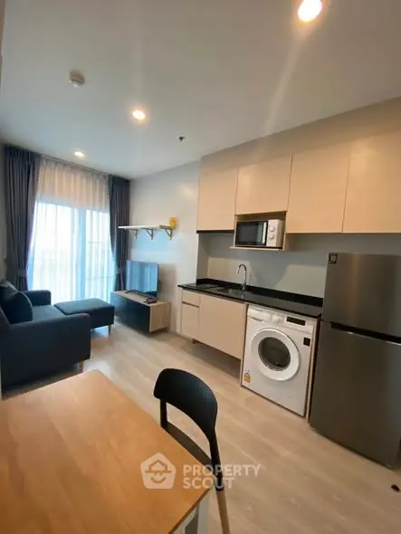 Modern open-layout living room with kitchen, featuring sleek appliances and cozy seating area.