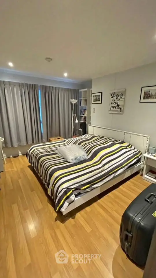 Cozy bedroom with striped bedding and wooden flooring, featuring modern decor and ample natural light.
