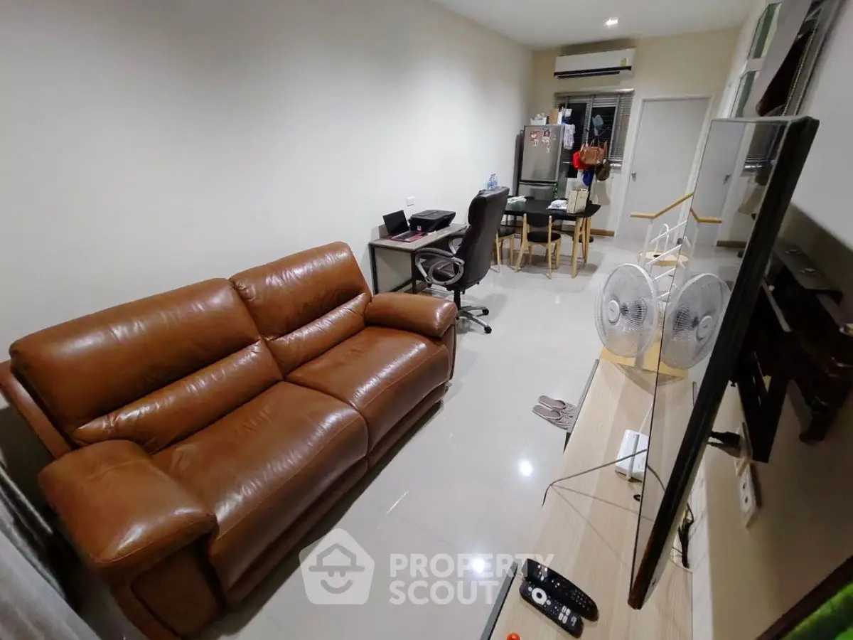 Modern living room with leather sofa, TV, and dining area in open layout apartment.