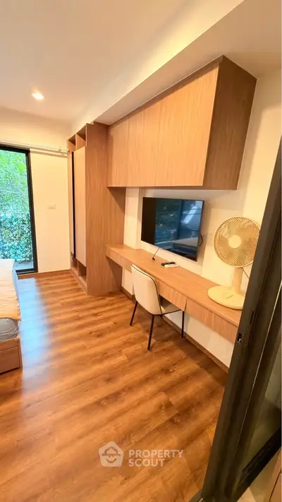 Modern bedroom with built-in desk and TV, featuring wood flooring and large window view.