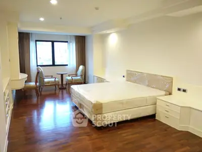 Spacious bedroom with hardwood floors, large window, and elegant furniture in a modern apartment.