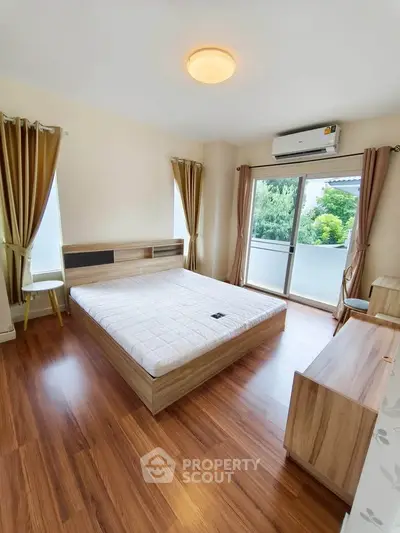 Spacious bedroom with wooden flooring and balcony access in modern apartment.
