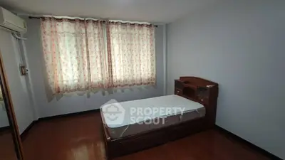 Cozy bedroom with wooden flooring and floral curtains, featuring a single bed and air conditioning.
