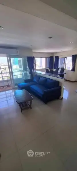 Spacious living room with modern blue sofa and large windows offering city views.