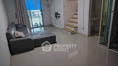 Modern living room with sleek sofa and staircase leading to upper level, featuring glossy tiled flooring.