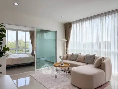 Modern living room with cozy sofa and large windows, adjacent to a bright bedroom with scenic views.