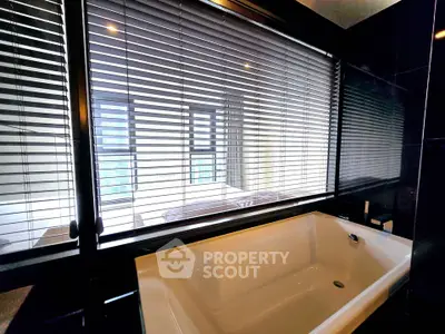 Luxurious bathroom with modern bathtub and large window with blinds, offering a serene ambiance.