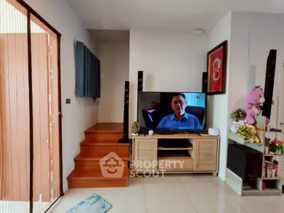 Cozy living room with modern TV setup and wooden staircase, perfect for relaxation and entertainment.